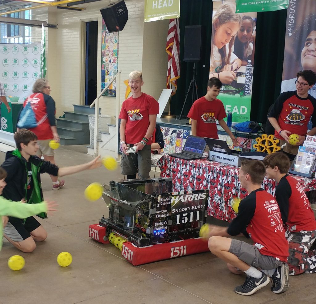 Team members at their booth at the New York State Fair with youth tossing balls to the robot