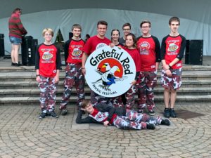 9 students in front of ampitheatre holding a round Grateful Red Musical Festival Sign