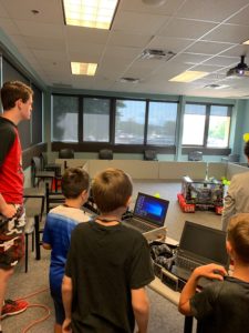 3 children standing behind laptops looking at a team robot