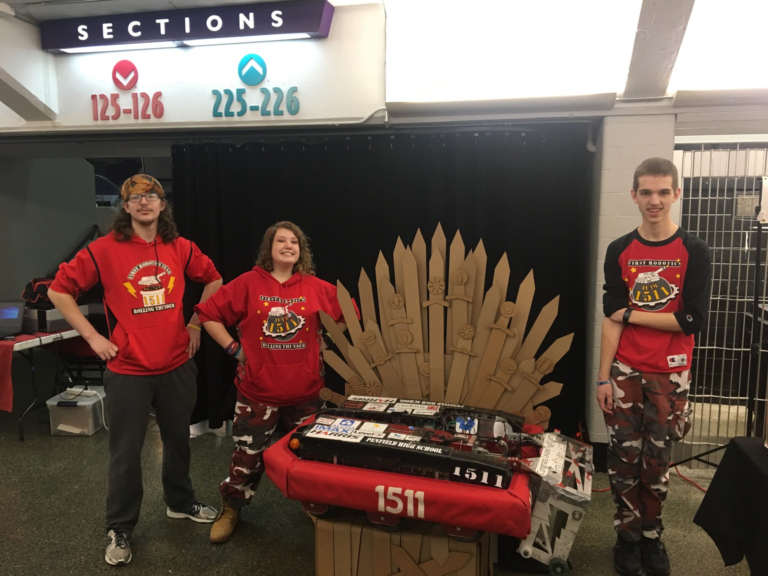 3 team members posing with robot sitting on a cardboard throne at Comic Con