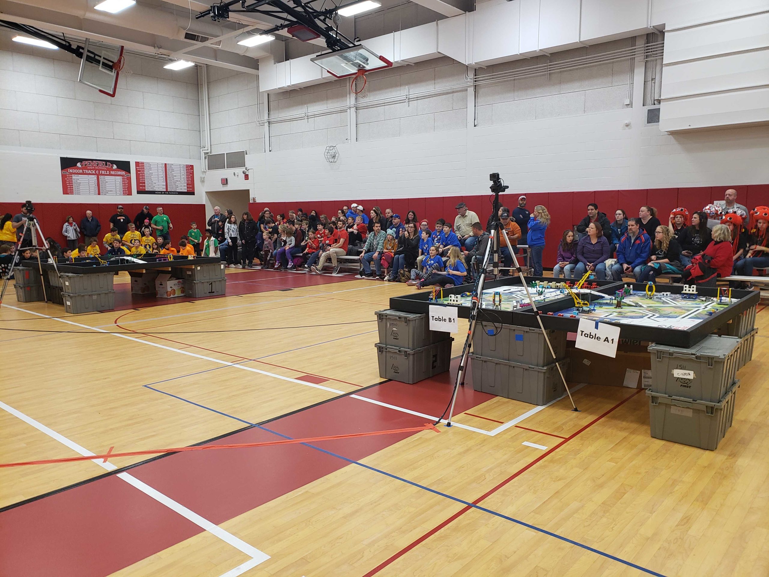 A gymnasium filled with FLL robotics teams, playing fields and spectators