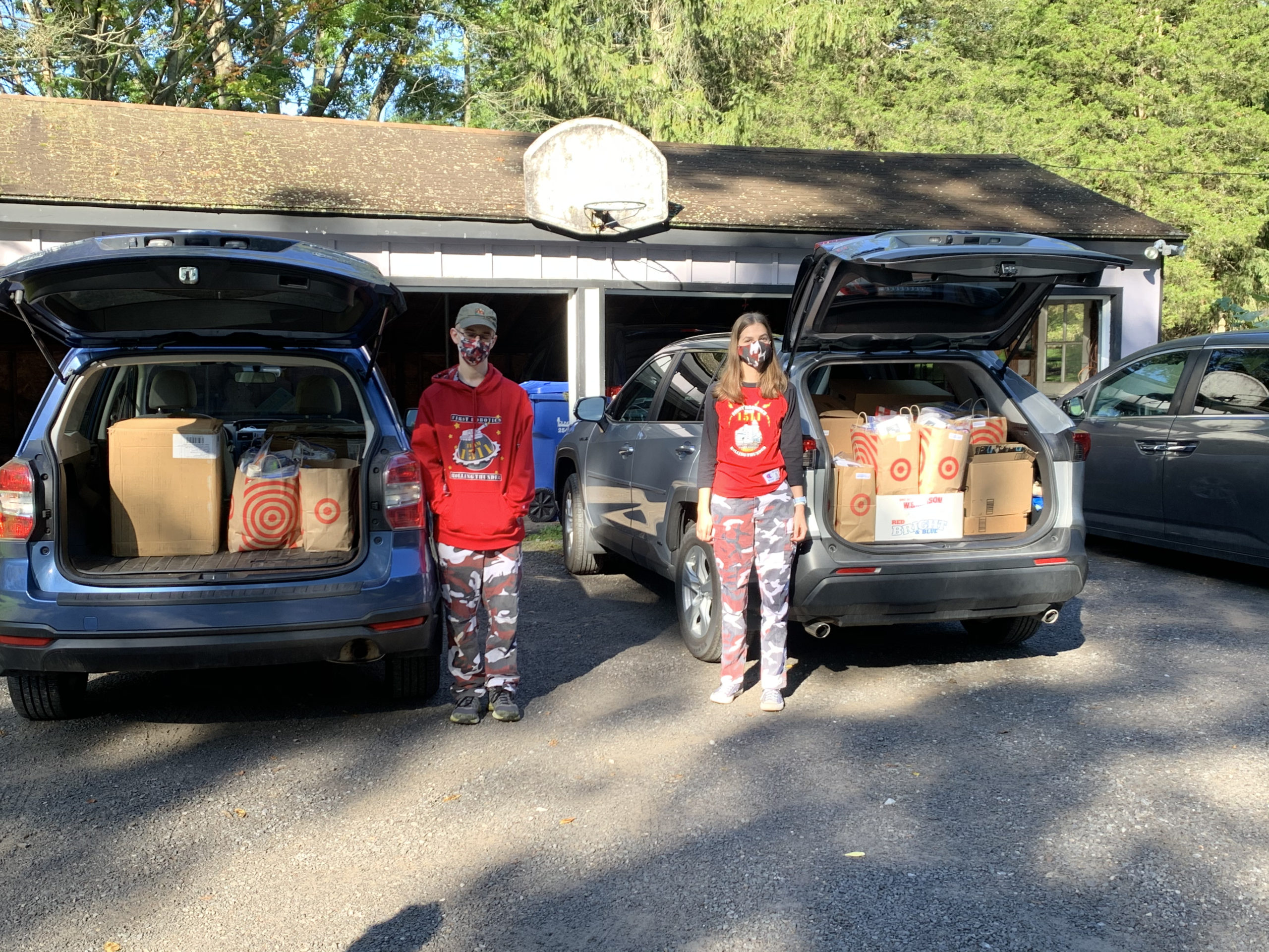 2 team members standing in front of 2 cars with trunks full of items for Happy Birthday Cha Cha Cha