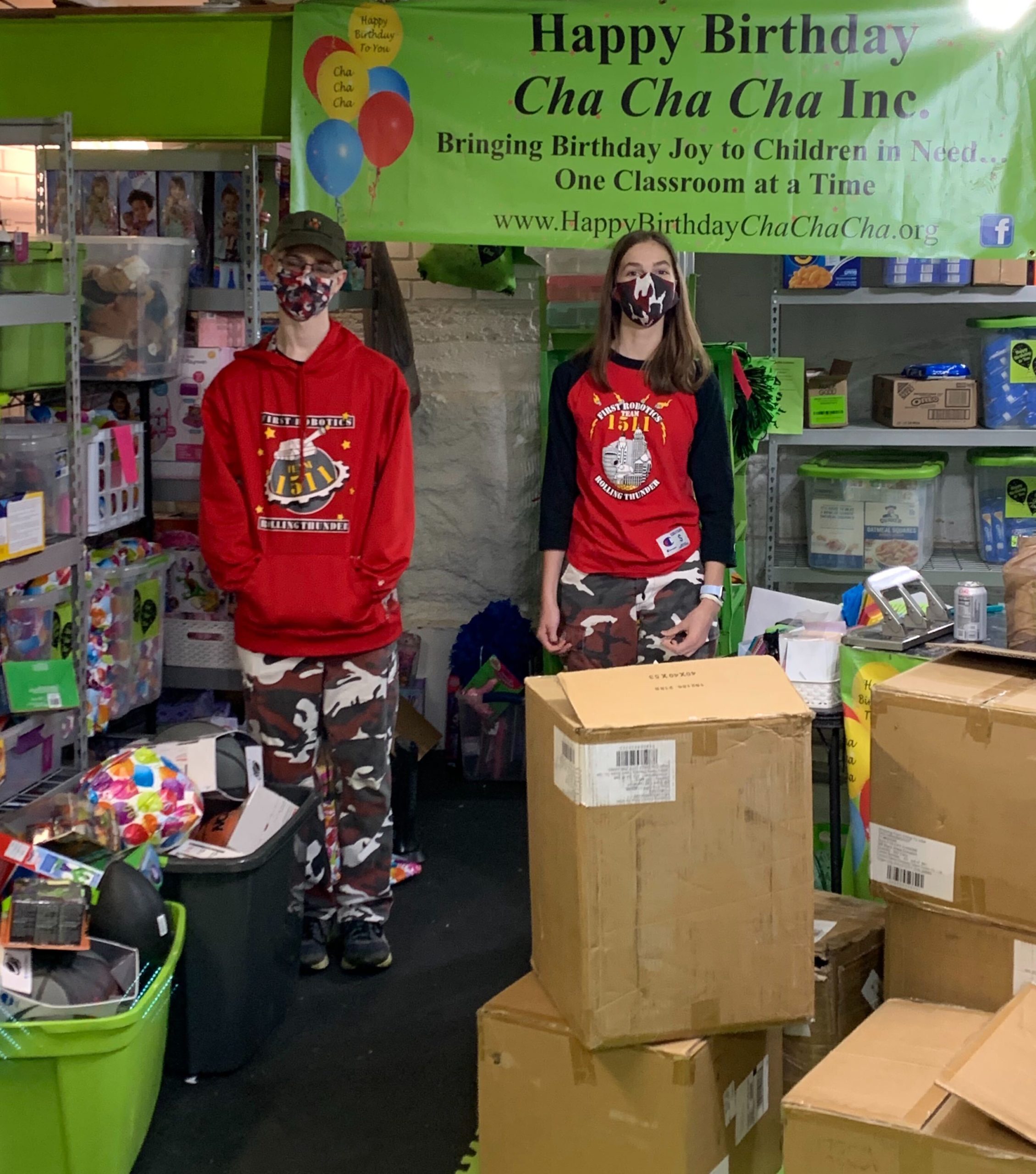 2 students standing in front of Happy Birthday Cha Cha Cha Sign with boxes of donations for Happy Birthday Cha Cha Cha