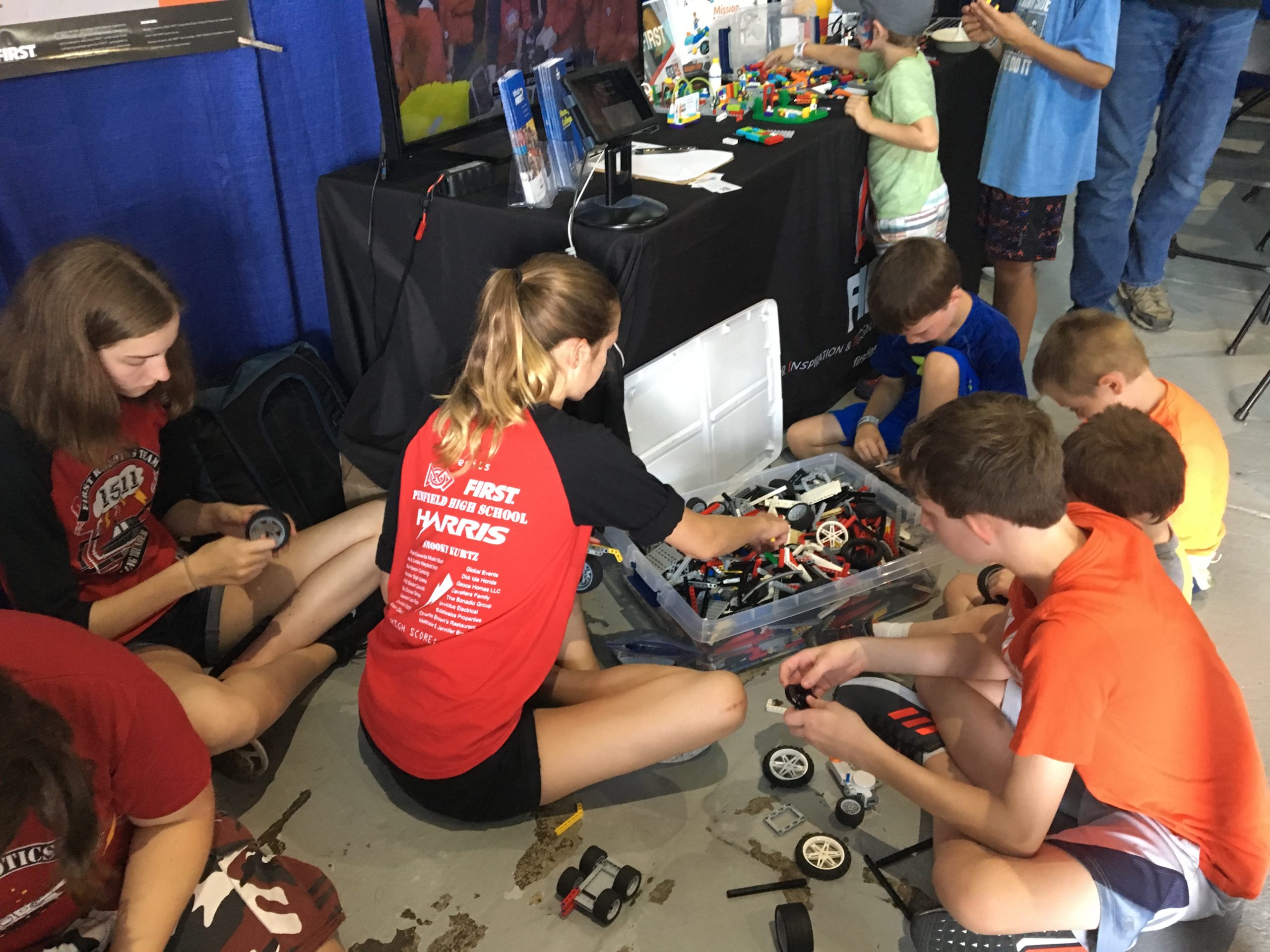 Team member sitting on floor with youth spectators building robots at New York State Fair